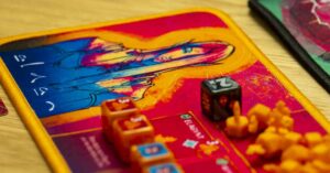 Ein farbenfrohes Brettspiel-Tableau mit einer Illustration einer Figur in der Mitte, umgeben von verschiedenen Spielwürfeln und kleinen orangefarbenen Spielfiguren auf einem Holztisch.